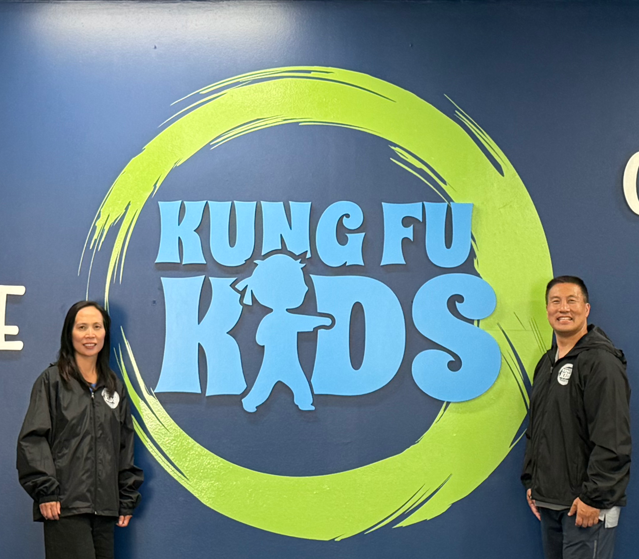 Sifu Liz and Sifu Chang stand next to the Kung Fu Kids logo